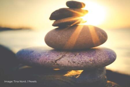 Stacked smooth stones on a beach with a beautiful sunset in the background. The warm sunlight creates a serene and tranquil atmosphere, highlighting the balance and harmony of the stones. Image by Tina Nord from Pexels.